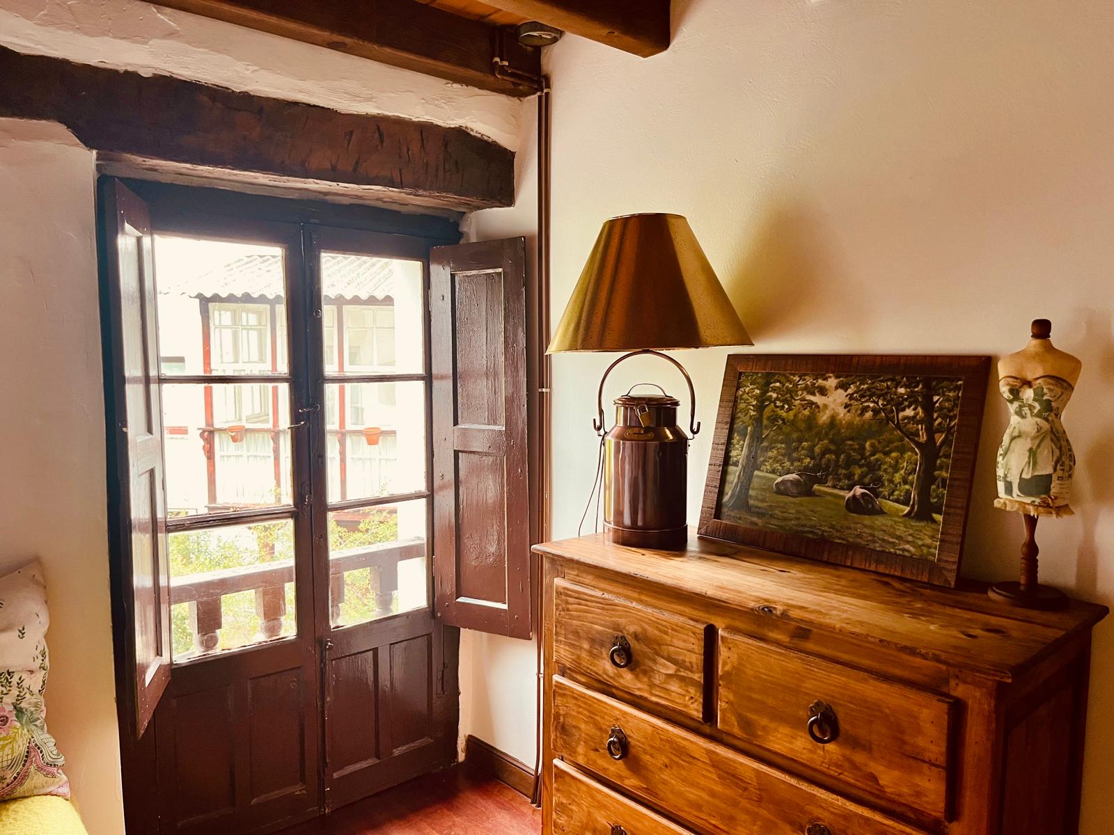 Dormitorio con cómoda de madera y ventana al patio en casa rural cántabra