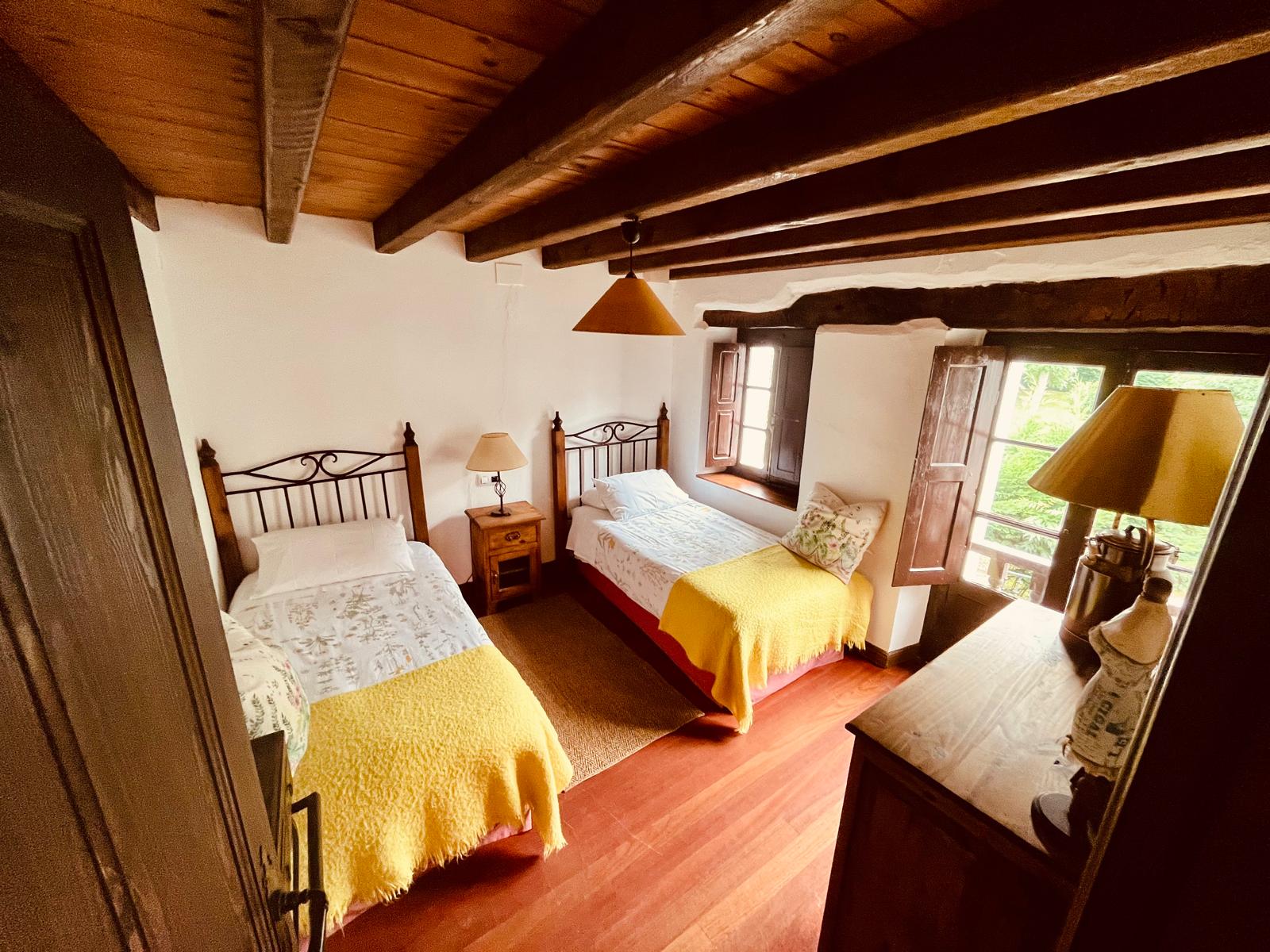 Habitación doble con dos camas individuales y vigas de madera en casa rural de Cantabria